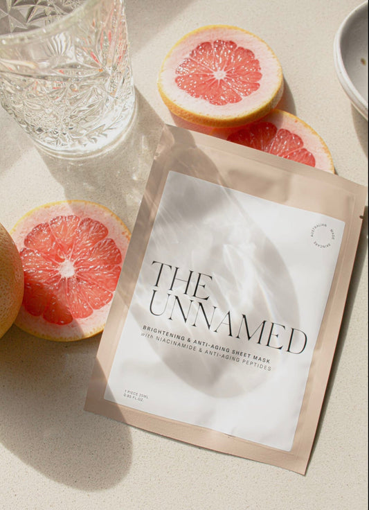 The Unnamed Brightening & Anti-Aging Sheet Mask styled flatlay with grapefruit slices on a light surface.