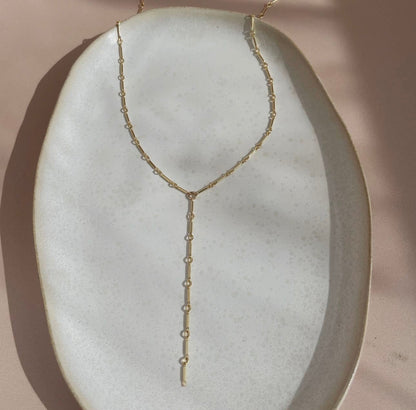 Token Jewelry Dot and Dash Lariat necklace in gold displayed on a ceramic dish.