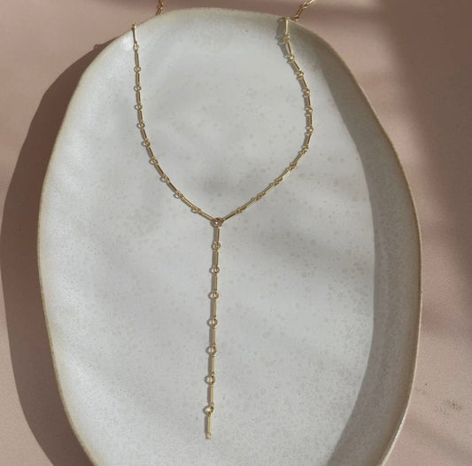 Token Jewelry Dot and Dash Lariat necklace in gold displayed on a ceramic dish.