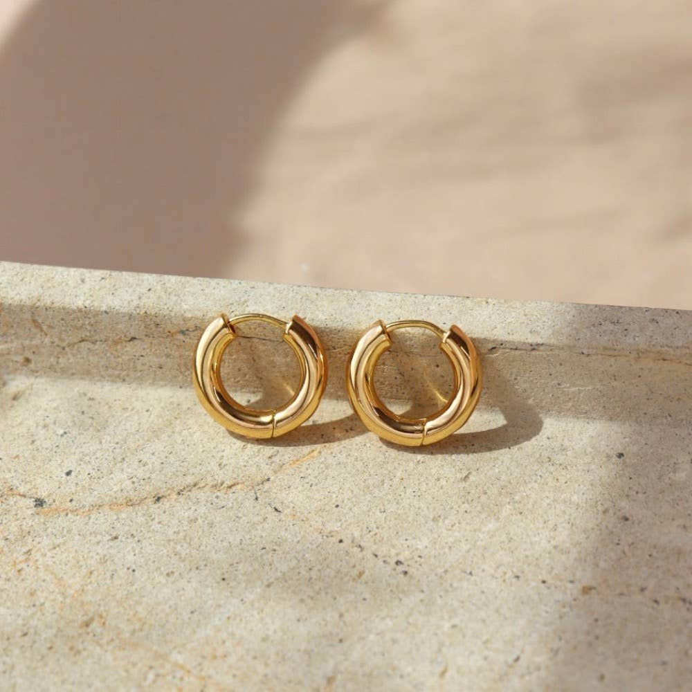Token Jewelry Everyday Hoops gold earrings displayed on a stone surface with soft natural light.