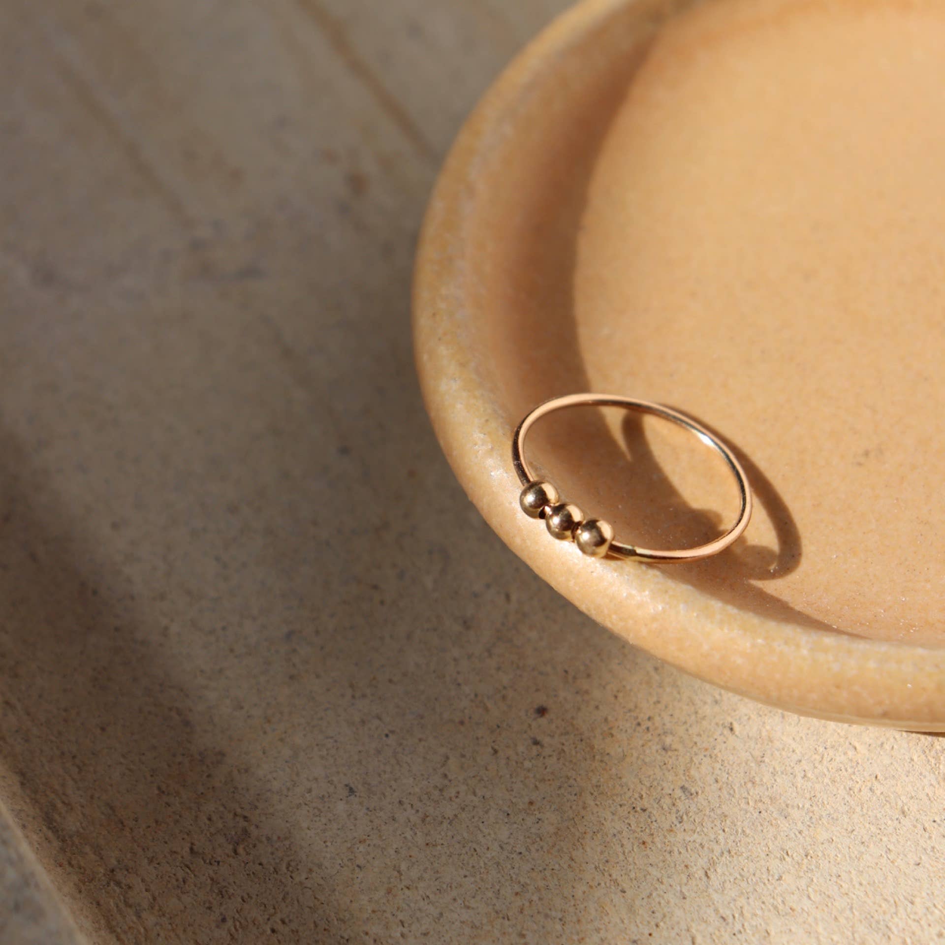 Gold Token Jewelry Meridian Fidget Ring styled in a yellow dish, captured in warm moody lighting.