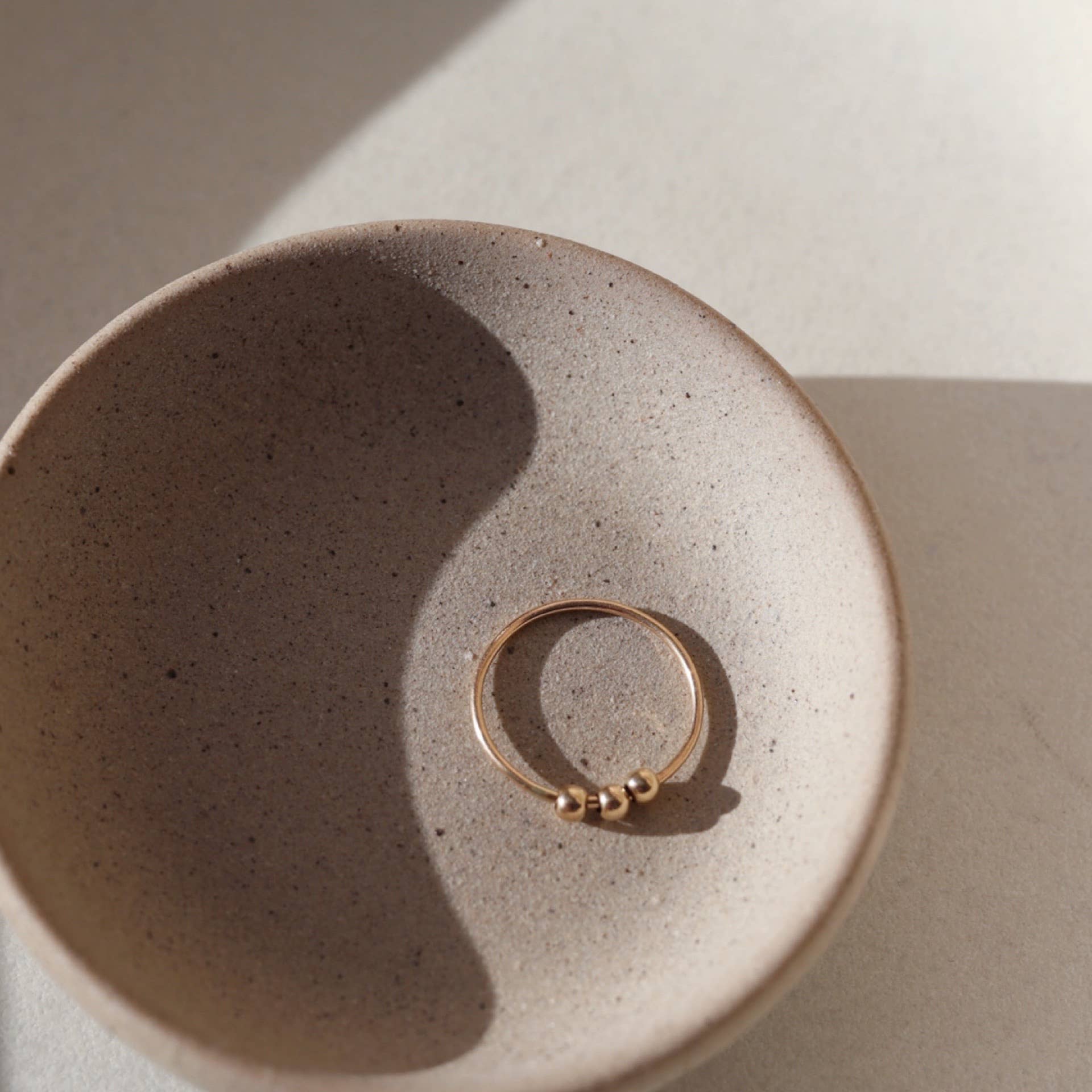 Gold Token Jewelry Meridian Fidget Ring placed in a speckled ceramic bowl, photographed with soft shadowing.