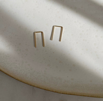 Close-up of Token Jewelry Mini Staples earrings in gold on a textured dish.