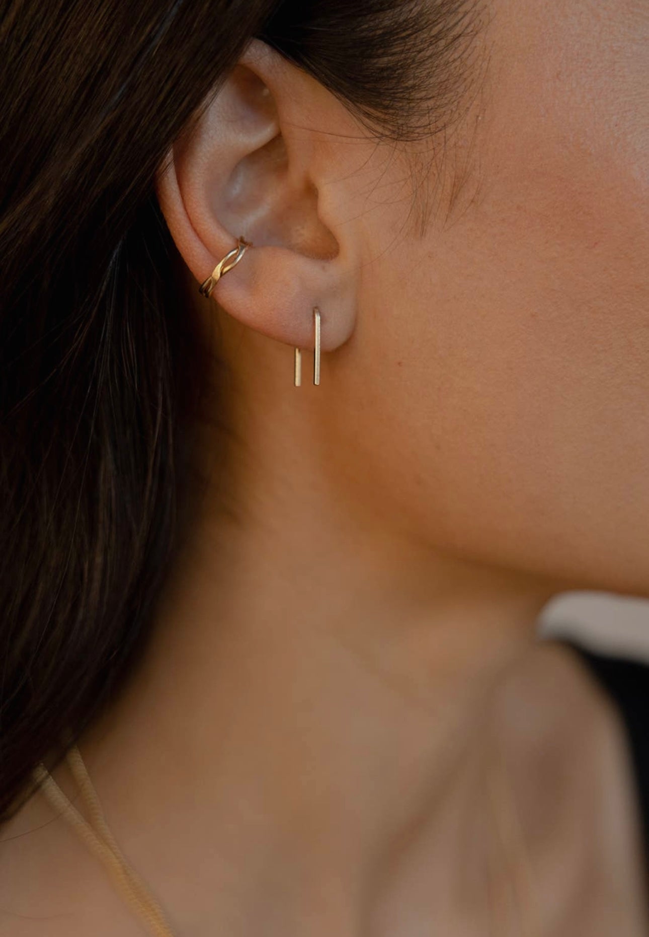 Model wearing Token Jewelry Mini Staples earrings in gold, side view.