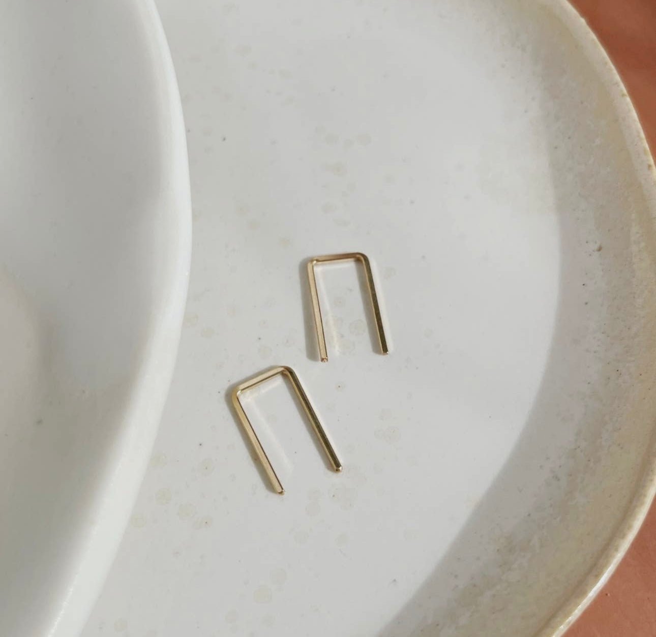 Token Jewelry Mini Staples earrings in gold displayed on a ceramic dish.