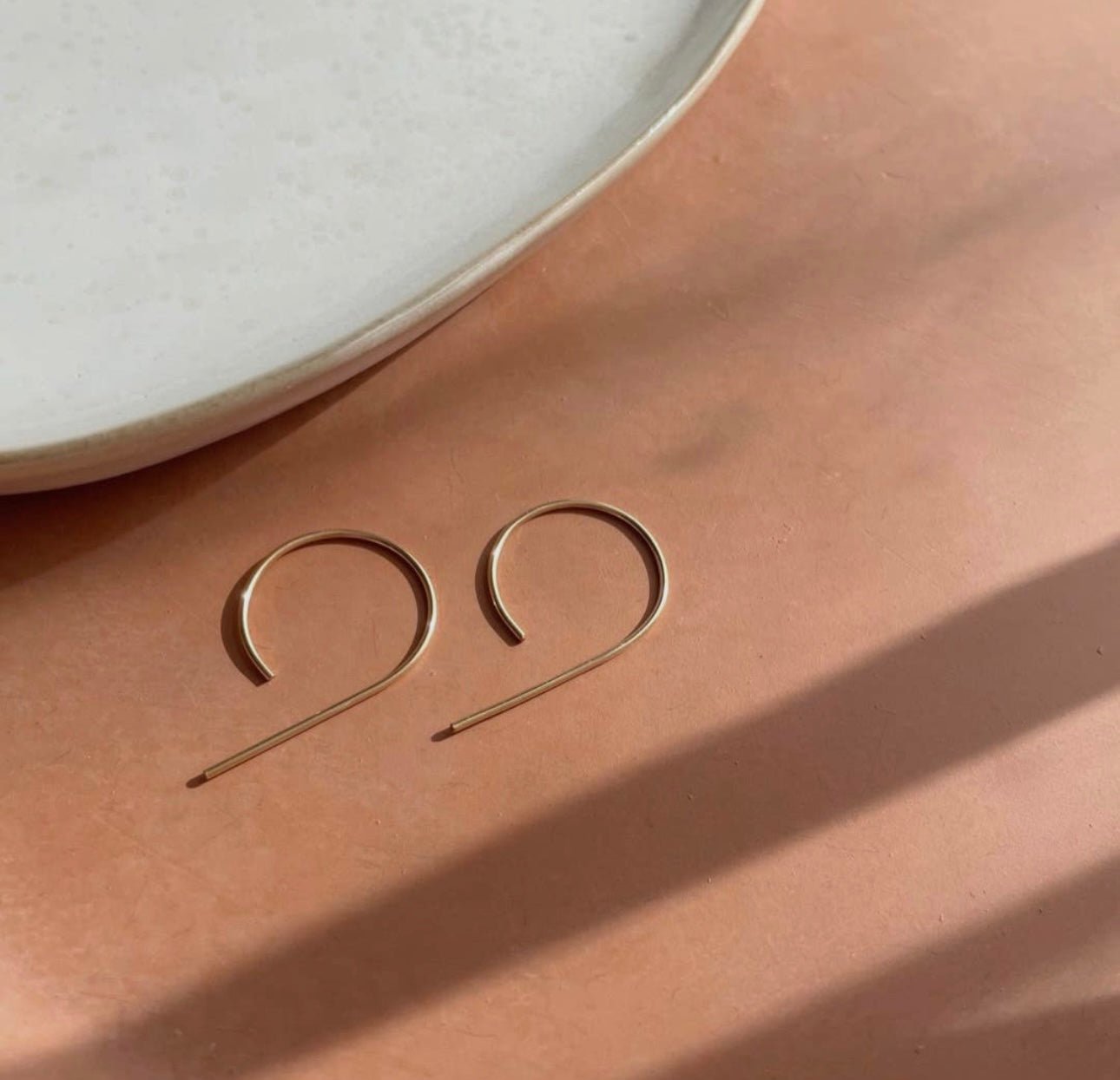 Token Jewelry The Nines earrings in gold flatlay on a peach-toned surface.