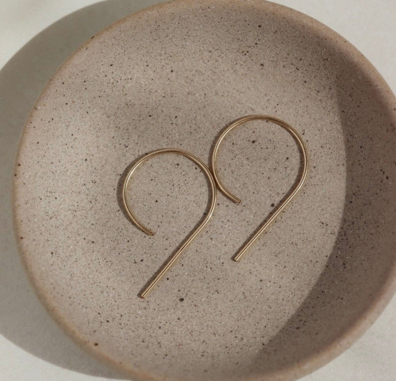 Token Jewelry The Nines earrings in gold displayed on a neutral ceramic dish.