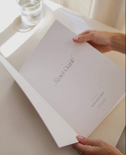 Person unboxing The Reset Guide by Wilde House Paper, opening to the first page at a sunlit table.