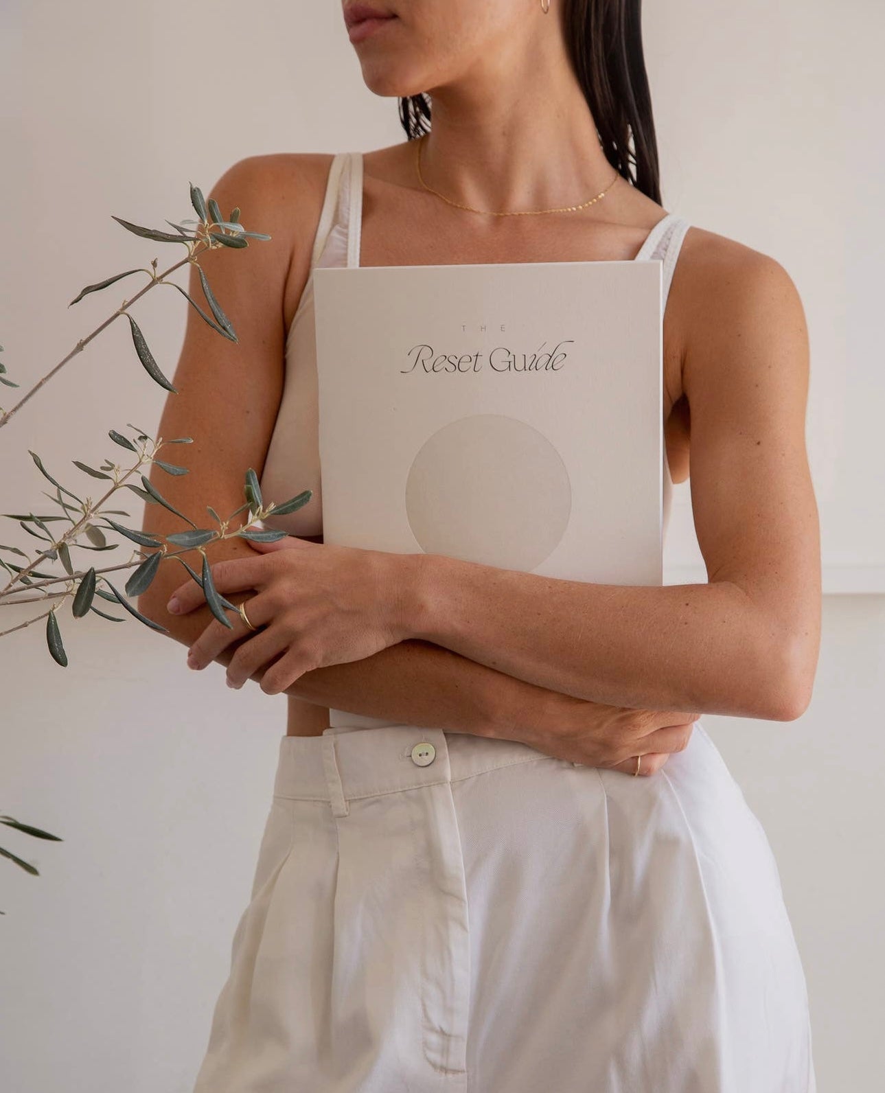 Model dressed in white holding The Reset Guide by Wilde House Paper against her chest, minimal background.