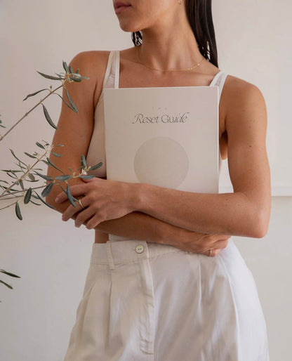 Model dressed in white holding The Reset Guide by Wilde House Paper against her chest, minimal background.